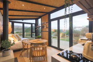 Aardvark: bed and round dining table beside glass walls, SMEG kettle on the counter, Old Mac Daddy, Elgin Valley
