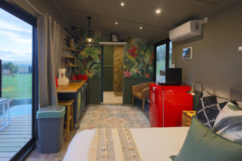 Kaapse Nooi: bed, kitchenette and red SMEG fridge below a tropical mural, Old Mac Daddy, Elgin Valley
