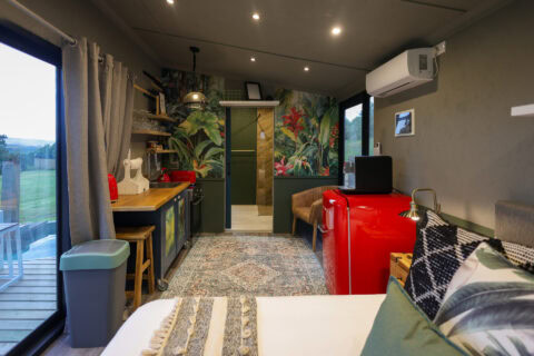 Kaapse Nooi: bed, kitchenette and red SMEG fridge below a tropical mural, Old Mac Daddy, Elgin Valley