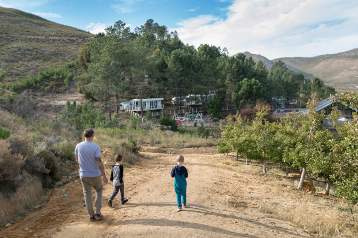 A man and two boys walking up a dirt road between apple trees towards the Airstreams on the hillside, Old Mac Daddy, Elgin Valley
