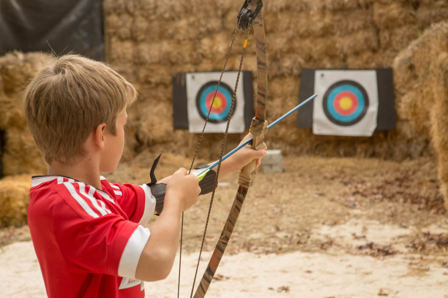 A boy aiming a bow at a target set against hay bales, Old Mac Daddy, Elgin Valley