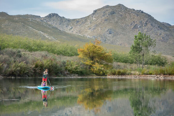 A child on a stand-up paddle board on a still pond below the mountains, Old Mac Daddy, Elgin Valley