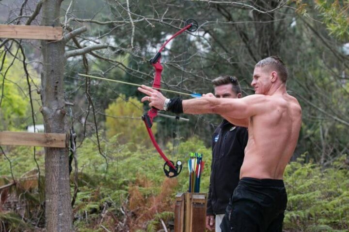 Two men at archery, one drawing a red bow in the pine trees, Old Mac Daddy, Elgin Valley