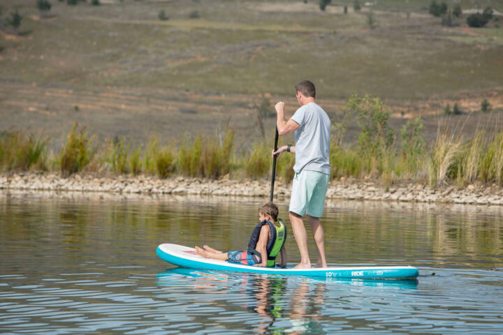 A man paddle boarding on the lake with a boy sitting at the front of the board, Old Mac Daddy, Elgin Valley