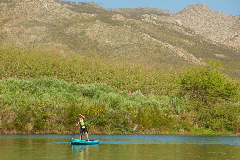 A person on a stand-up paddle board below green slopes and mountains, Old Mac Daddy, Elgin Valley