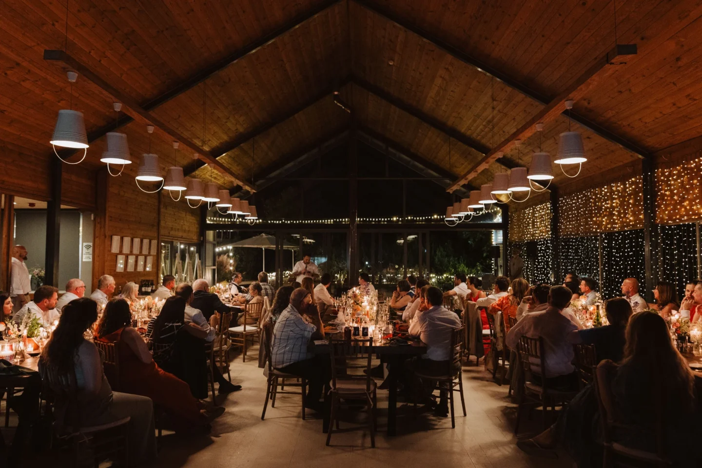 Guests at dinner at long tables in the Barn in the evening, lights strung overhead, Old Mac Daddy, Elgin Valley