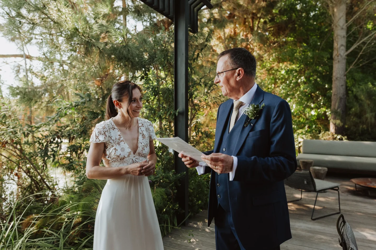 Bride reading from a sheet of paper beside an older man in a navy suit on a covered deck, Old Mac Daddy, Elgin Valley