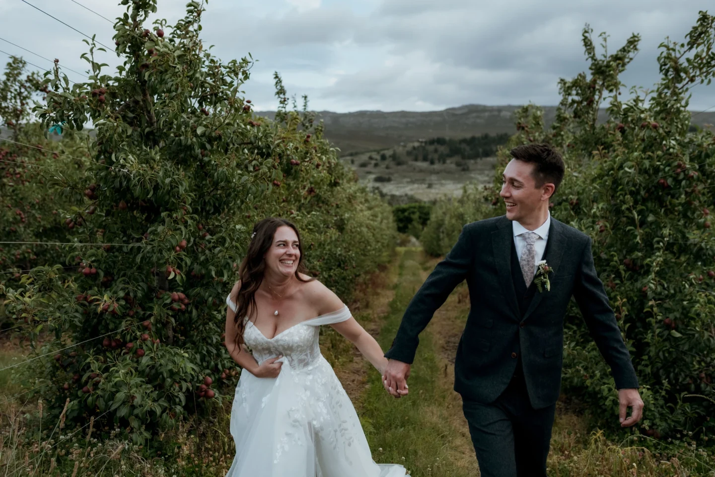 Bride and groom walking hand in hand between the rows of the apple orchard, Old Mac Daddy, Elgin Valley