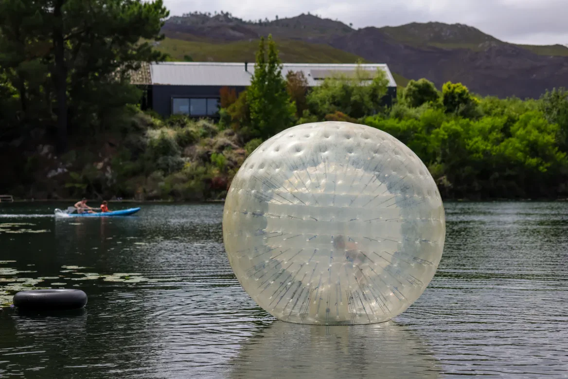 Team Building Water zorb floating on the lake, a kayaker and the lodge behind, Old Mac Daddy, Elgin Valley