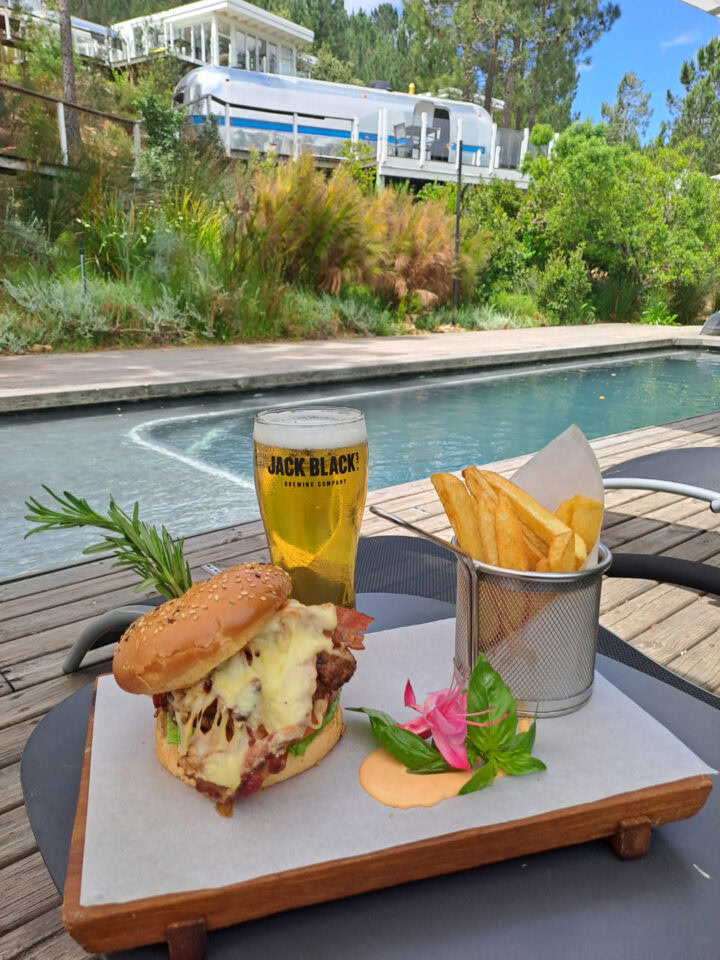 A burger, fries and a beer on a board beside the pool, with an Airstream on the hill behind, Old Mac Daddy, Elgin Valley