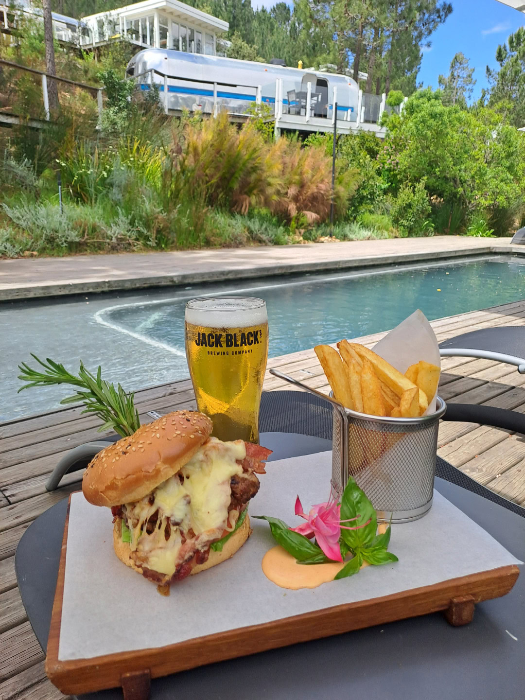 A burger, fries and a beer on a board beside the pool, with an Airstream on the hill behind, Old Mac Daddy, Elgin Valley