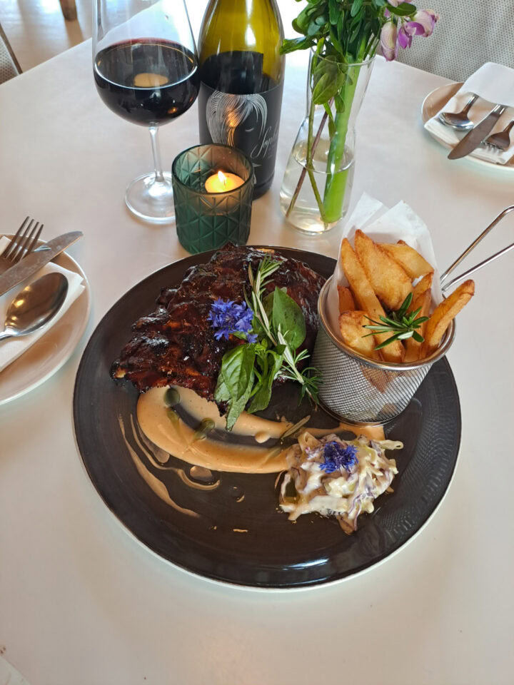 A glazed meat dish with fries in a cone and coleslaw, beside a glass of red wine, Old Mac Daddy, Elgin Valley