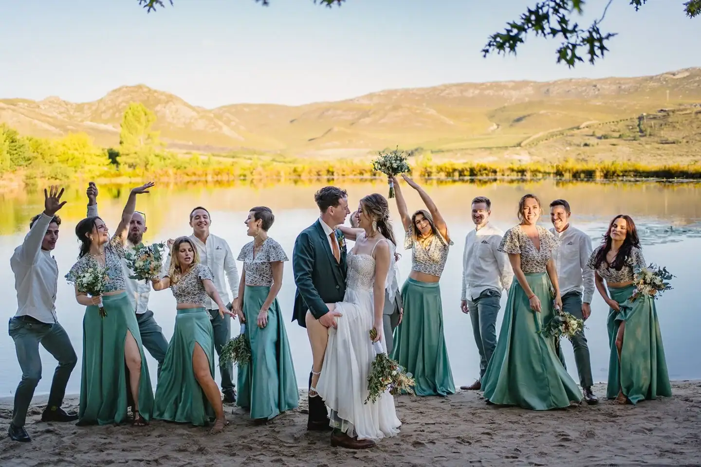 Bridal party celebrating on the lakeside beach, bouquets in the air, mountains across the water, Old Mac Daddy, Elgin Valley