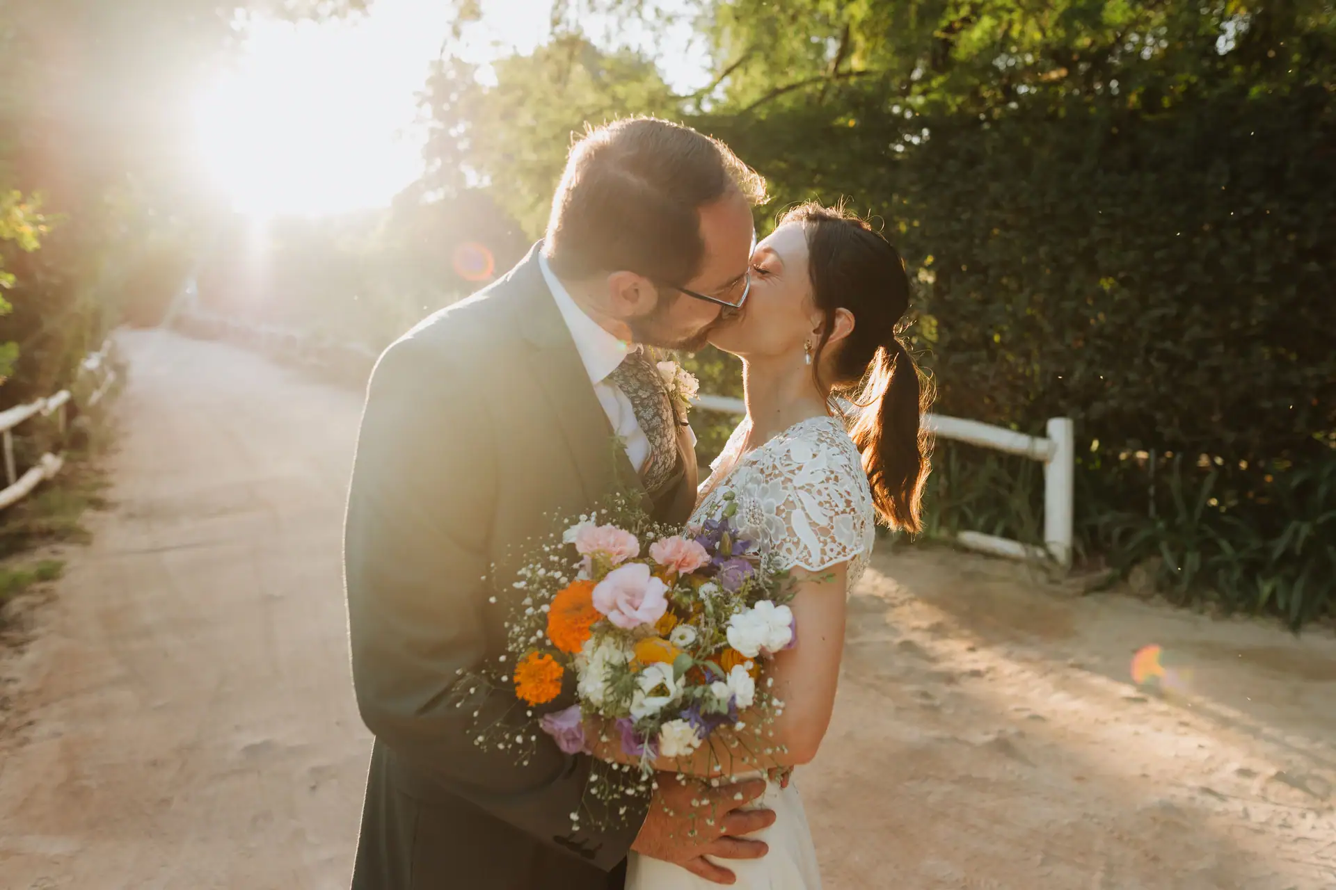 Bride and groom kissing on a sunlit lane, a wildflower bouquet in her hand, Old Mac Daddy, Elgin Valley