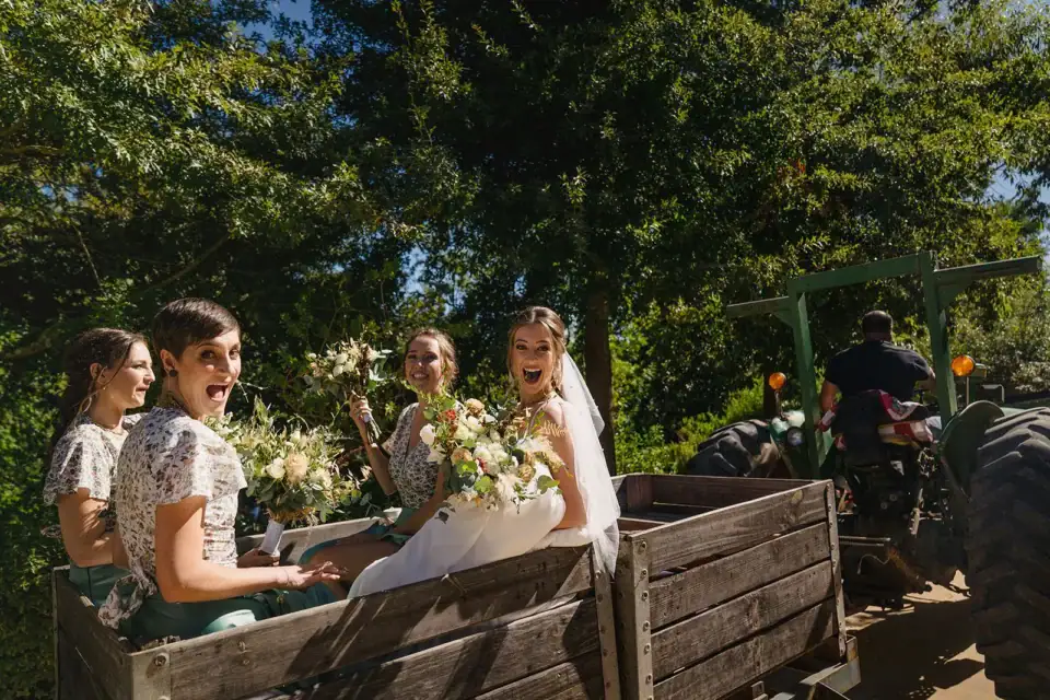 Weddings & Events Bride and bridesmaids laughing in a trailer pulled by a green tractor, Old Mac Daddy, Elgin Valley