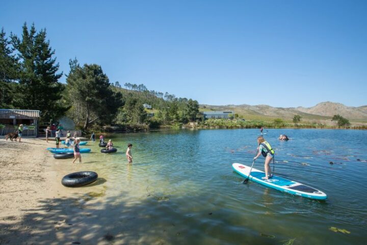 A paddle boarder on the lake, with swimmers and inner tubes by the beach, Old Mac Daddy, Elgin Valley