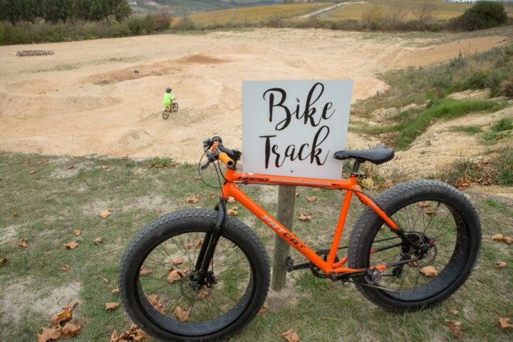 An orange fat-tyre bike parked beside the Bike Track sign, Old Mac Daddy, Elgin Valley