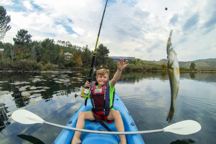 A boy in a kayak holding up a fish he has just caught, Old Mac Daddy, Elgin Valley