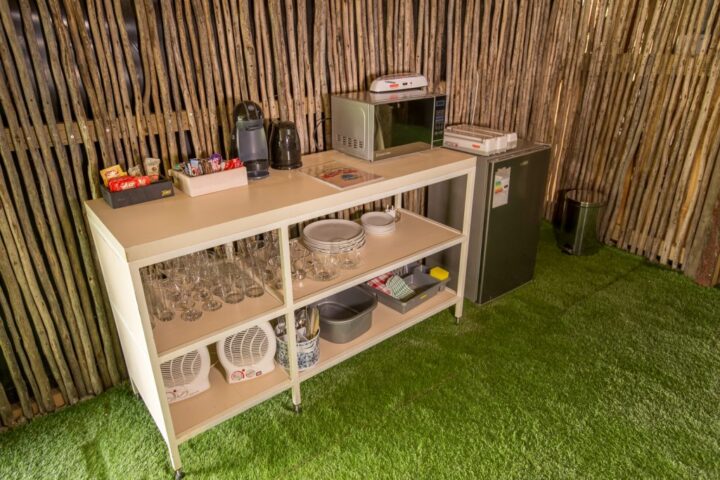 Camp kitchenette shelf with a kettle, microwave, crockery and a bar fridge against a reed wall, Old Mac Daddy, Elgin Valley
