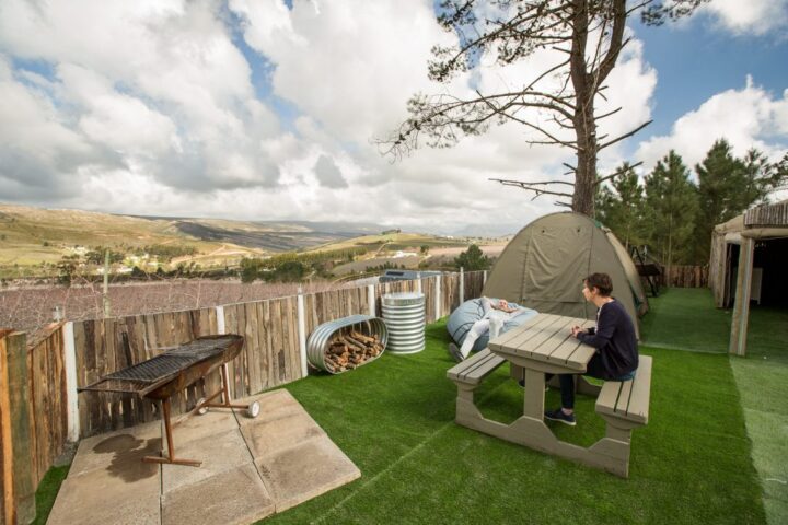 A guest at a picnic table beside a braai and a dome tent on artificial grass, Old Mac Daddy, Elgin Valley