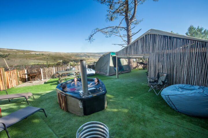 Campsite with a wood-fired hot tub, loungers and dome tents behind a reed fence, Old Mac Daddy, Elgin Valley