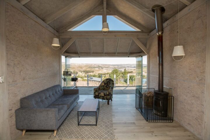 Villa lounge with a grey sofa and a wood stove, glass doors opening onto the view, Old Mac Daddy, Elgin Valley