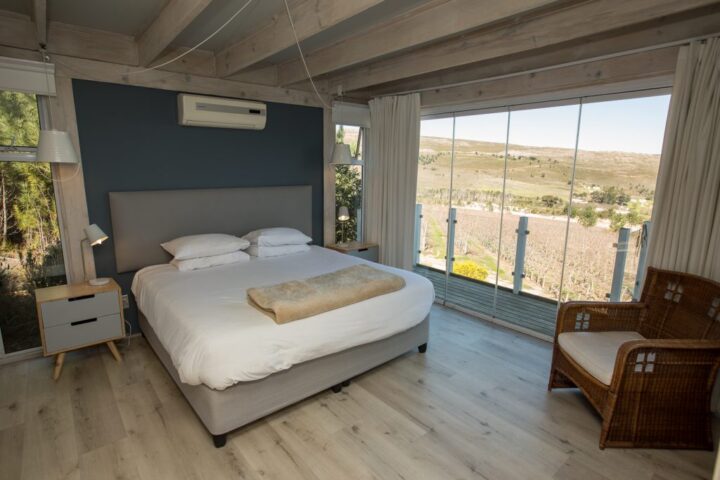 Villa bedroom with a double bed, a wicker chair and a glass wall onto the vineyards, Old Mac Daddy, Elgin Valley